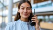 © ISVO - Female security guard in gray uniform using a walkie-talkie, smiling while standing in a modern building with large windows and a bright interior