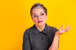 © deagreez - Mature woman with glasses and gray hair making a confused shrug on bright yellow background expressing doubt and disbelief