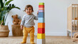 © Premium_art - Smiling toddler girl with brown hair playing with colorful stacking blocks indoors.