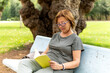 © ADDICTIVE STOCK - Senior woman reading on park bench enjoying outdoor leisure