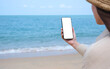 © Farknot Architect - Mockup image of a woman holding mobile phone with blank desktop screen by the sea