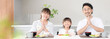 © kapinon - いただきますをしてダイニングで座る食事を始める親子3人の家族・食育や家族団らんのカメラ目線イメージバナー