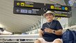 © Nazareno - Man traveling, waiting in airport terminal, using smartphone