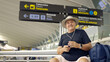 © Nazareno - Mature man smiling waiting flight holding smartphone at airport