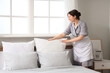 © Pixel-Shot - Beautiful young chambermaid fluffing pillows in stylish bedroom