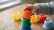 © SUHEB - A toddler hand stacking colorful plastic nesting cups on a wooden table, focusing on early childhood development and playful educational activities