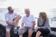 © luciano - Three senior adult friends sitting on a low wall near the sea, enjoying a casual conversation and connecting while spending time together outdoors