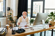 © LIGHTFIELD STUDIOS - A well-dressed older professional reviews paperwork thoughtfully in a bright, contemporary office space.