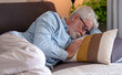 © luciano - Senior man with grey hair and beard napping comfortably on a modern sofa in his living room, embracing rest and peaceful retirement lifestyle at home