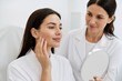 © Babb - A skincare expert stands behind a woman in a spa. The woman examines her reflection in a mirror while touching her face. The atmosphere is light and inviting.