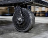 Scuffed and heavily dirty black rubber tire moving a heavy industrial trolley inside a warehouse