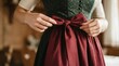 © SimpleDesignStudio - Young Woman Tying Red Apron Bow on Traditional Bavarian Dirndl Dress for Oktoberfest Celebration