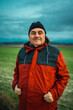 © Nazareno - Smiling man wearing red jacket standing outdoors in field