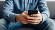 © Ariestia - Close-up of a Man's Hands Using a Smartphone for Texting and Browsing While Sitting on a Couch Indoors