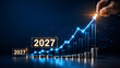 © Yuparet - Strategic planning for future growth is illustrated in this 2027 business montage with glowing upward arrow, stacked coins, and bar chart symbolizing financial success