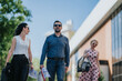 © qunica.com - Three adults in business casual attire walk together along a city street. A casual urban scene of colleagues walking outside near office buildings on a sunny day.