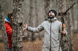 © qunica.com - Two friends gather branches in a pine forest while dressed in warm outdoor jackets. A man and woman explore the mountain woods, looking up and collecting firewood.