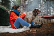 © qunica.com - A woman sits on a blanket outdoors hugging her large dog near a tent. Two friends enjoy a relaxed forest camping scene with a hammock in the background.