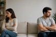 © Formoney - Two people sit on opposite ends of a couch in a living room. They have their arms crossed and show signs of disagreement. The atmosphere feels tense and unresolved between them.