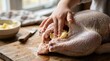 © velikiyzayats - Close up of a person preparing a raw turkey for roasting by rubbing butter under the skin on a wooden cutting board in a rustic kitchen for Thanksgiving dinner preparation