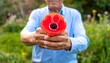 © Verse - Person in white shirt holding vivid red poppy flower with both hands, green foliage background, outdoor natural setting highlighting contrast and delicate texture.