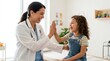 © Alva - Smiling female doctor giving a high-five to a happy young girl during a friendly medical check-up in a bright clinic room.