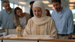 © AnastasiiaRozhmanova - Berber Muslim woman in office hijab decorates her cubicle with a small Eid lantern, colleagues of varied backgrounds leaning over curiously, fluorescent workplace lighting,