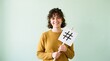 © Cliff - Smiling young Asian woman holding a hashtag symbol against a bright background. Social media marketing, networking, trending topic, and minimalist lifestyle concept