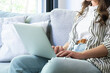 © simona - Young woman working on a laptop while sitting on a sofa at home, a casual remote work scene in a bright living room showing comfort, focus and modern freelance productivity