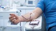 © Natali - A person sits in a chair at a donation center with a blood bag on their side and a needle in their arm. It is a common health event where blood is collected