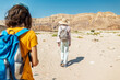© zhukovvvlad - A boy with a backpack and a map walks next to his mother through the desert. Family trekking. Timna National Park. The child is actively spending time.