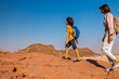 © zhukovvvlad - A boy with a backpack and a map walks next to his mother through the desert. Family trekking. Timna National Park. The child is actively spending time.