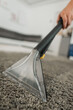 © Anastasia - Carpet cleaning extractor nozzle lifting dirt from gray carpet in bright indoor room with handheld tool, visible grip, clear suction chamber, damp fibers, and fresh cleaned surface