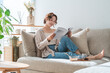 © buritora - A stylish Asian woman sitting on the living room sofa, reading a magazine during teatime.