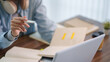 © snowing12 - Adult student holding pen while studying with notebook and laptop at wooden desk during online learning session