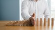 © Caleb - Hand stopping falling wooden dominoes representing risk management, crisis intervention and business protection strategy to prevent chain reaction failure.