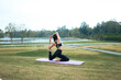 © PaeGAG - Woman performing a yoga pose on a mat in a park by a lake