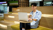 © Stella 16 - Young Asian Man Working on Laptop with Coffee Cup at Modern Mall Seating Area