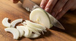 ©  CREATIVE ARTWORK - Closeup of a chefs hand slicing a fresh white onion on a wooden cutting board in a kitchen