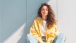 © anjas - Woman with curly hair in yellow shirt sitting by wall.
