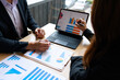 © Phushutter - Two business professionals discussing sales charts and graphs on a laptop and paper reports during a team meeting at a desk in a modern office.