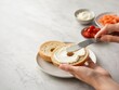 © Serjio - Preparación de un bagel con crema y ingredientes frescos en la mesa de cocina