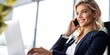 © FrameShift - Attractive blonde businesswoman talking on phone while working on laptop in modern office