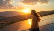 © Ketikan - A woman stands on a rooftop with solar panels overlooking a mountainous landscape at sunset