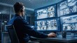 © Taras Roshchuk - A worker sits at a desk in a control room. He is wearing a headset and watching multiple security screens. The screens show different views of a warehouse area