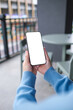 © Farknot Architect - Vertical mockup image of a woman holding and using mobile phone with blank desktop screen in cafe