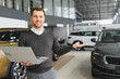 © Serhii - car seller standing in car salon and waiting for customers to come on sale