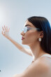© SHOTPRIME STUDIO - Profile of a stylish woman wearing transparent glasses and pearl earrings. She extends her arm forward against a soft light background. Concept of beauty, fashion, and elegance.
