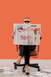 © Pixel-Shot - Woman in sunglasses holding a fashion newspaper with 'coming soon' text, sitting on an office chair against an orange background