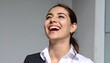 © Gundol - Young woman in blazer, gleefully looking upwards, smiling widely, with bright, genuine happiness against a gray wall
